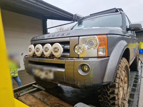 Schlammiger Land Rover Discovery mit Zusatzscheinwerfern auf dem Tieflader